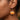 Close-up of a person's ear wearing a dangling pumpkin-shaped earring in bright orange with clear rhinestone trim and a gold hook.