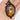 A hand holding an oval pendant necklace with a black ornate frame and a stained-glass-style autumn scene featuring a pumpkin, leaves, and a white letter 'O' in the center.