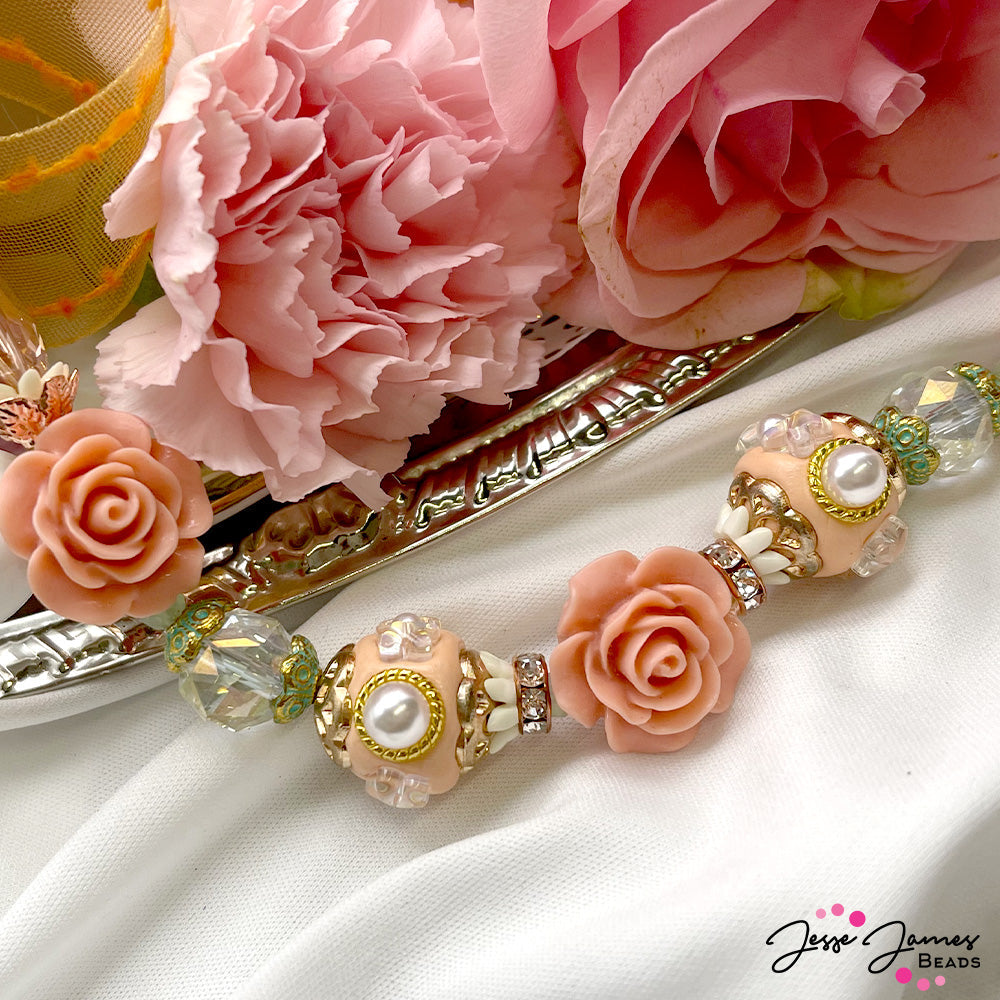 Create an elegant statement with this alluring peach and light green beads. This duo of bead strands features peach boho beads, faceted glass, patina metal bead findings, rose gold-plated metal components, peach acrylic roses, faceted glass hearts, and more. Show off your sassy smarts and warm heart with this beautiful duo of seven-inch bead strands. The largest bead in this set measures 18mm x 21mm. The smallest bead in this set measures 6mm x 2mm.