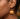 Close-up of a person's ear wearing a dangling pumpkin-shaped earring in bright orange with clear rhinestone trim and a gold hook.
