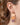 A close-up of a person's ear wearing a dangling earring with three hand-painted pumpkin charms in peach, orange, and muted purple, suspended from gold-toned metal.