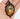 A hand holding an oval pendant necklace with a black ornate frame and a stained-glass-style autumn scene featuring a pumpkin, leaves, and a white letter 'O' in the center.