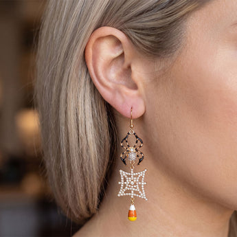 A close-up of a woman's ear wearing a dangling Halloween earring with a gold spider, a white pearl web, and a small candy corn charm.