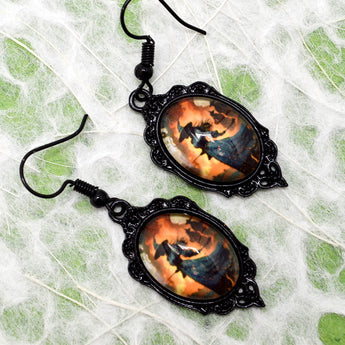 A pair of gothic-style dangle earrings with ornate black metal frames and horse-themed cabochon charms, displayed on a white web-like fabric background.