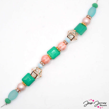 This 7 inch bead strand features faceted glass in pink, light blue, and teal colors. Includes rose-gold plated caged crystals, spacers, and rhinestone spacers. Largest bead on strand measures 13mm x 12mm x 7mm. Smallest bead measures 7mm x 2mm.