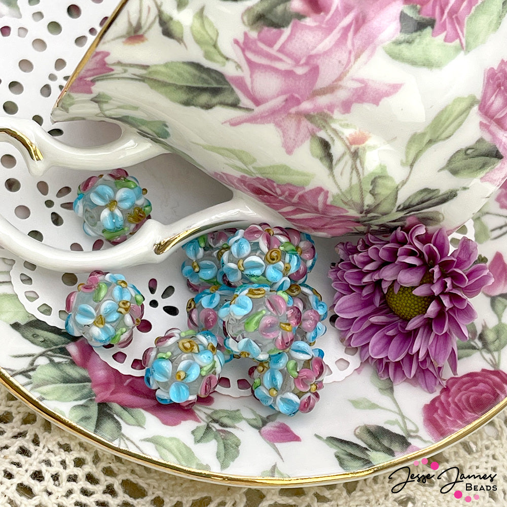 Don't sneak away to the gardens with that handsome gent yet! This beautiful lampwork style bead features a beautiful floral pattern perfect for creating garden party-worthy jewelry. Each bead features a colorful bouquet of blue and pink flowers with lush green leaf accents. 1 Bead per set. Measures 11mm.